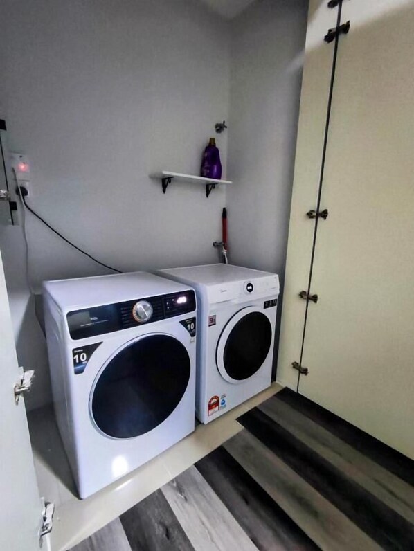 A laundry room with two washing machines, a shelf with toiletries, and a wooden floor.