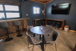 A bar area with a round table, bar stools, and a TV mounted on the wall.