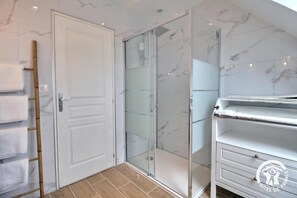A bathroom with a glass shower enclosure, a white door, and a towel rack with folded towels. - The Oasis Spa - PENVENAN (PENVENAN)