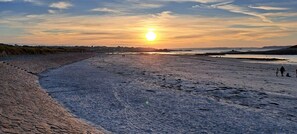 Ein Strand mit Sonnenuntergang, einem gepflasterten Weg und einer fernen Küste.