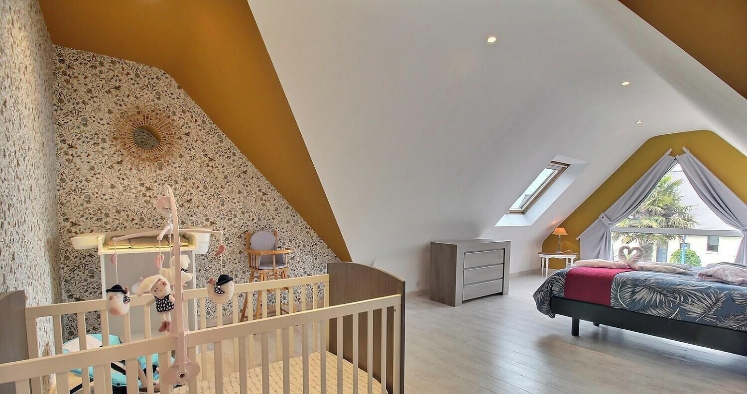 A bedroom with a sloped ceiling, a crib, a bed, and a window.
