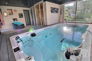 A modern indoor swimming pool with a hot tub, surrounded by a minimalist interior with artwork and a large window. - The Oasis Spa - PENVENAN (PENVENAN)