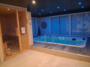 A spa area with a hot tub, wooden flooring, and a glass-enclosed sauna. - The Oasis Spa - PENVENAN (PENVENAN)