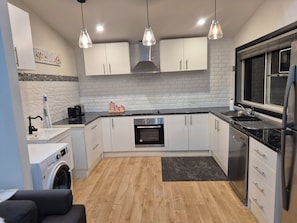 A modern kitchen with white cabinets, a built-in oven, a stainless steel refrigerator, and pendant lighting.