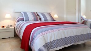 Uma cama com roupa de cama listrada e um cobertor vermelho, uma mesa de cabeceira com abajur e uma obra de arte pendurada na parede.