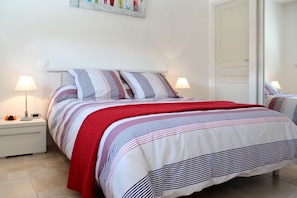 A bed with striped bedding and a red throw, a bedside table with a lamp, and a wall-mounted artwork. - A Green Oasis - PLOUHA (PLOUHA)