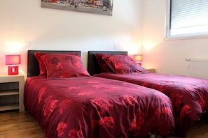 Ein Schlafzimmer mit zwei Betten, jeweils mit roter Blumenbettwäsche, Nachttischlampen und einem Bild an der Wand.