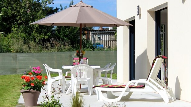 Um pátio externo com mesa, cadeiras, um vaso de planta e um guarda-sol grande.