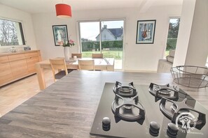 A modern kitchen with a central island, wooden cabinets, and a dining area with a table and chairs. - A Green Oasis - PLOUHA (PLOUHA)
