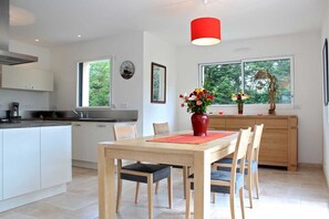 Eine moderne Küche mit weißen Schränken, einem Holztisch und Stühlen. Über dem Tisch hängt eine rote Pendelleuchte.