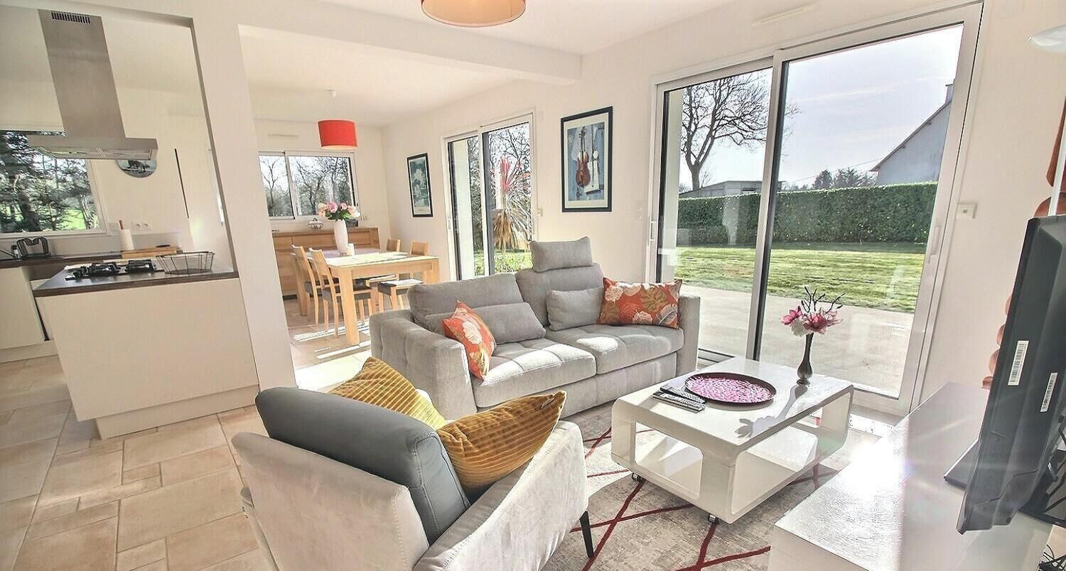 A modern living room with a grey sofa, a coffee table, and a dining area in the background.