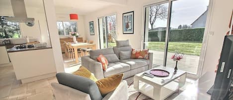 A modern living room with a grey sofa, a coffee table, and a dining area in the background.