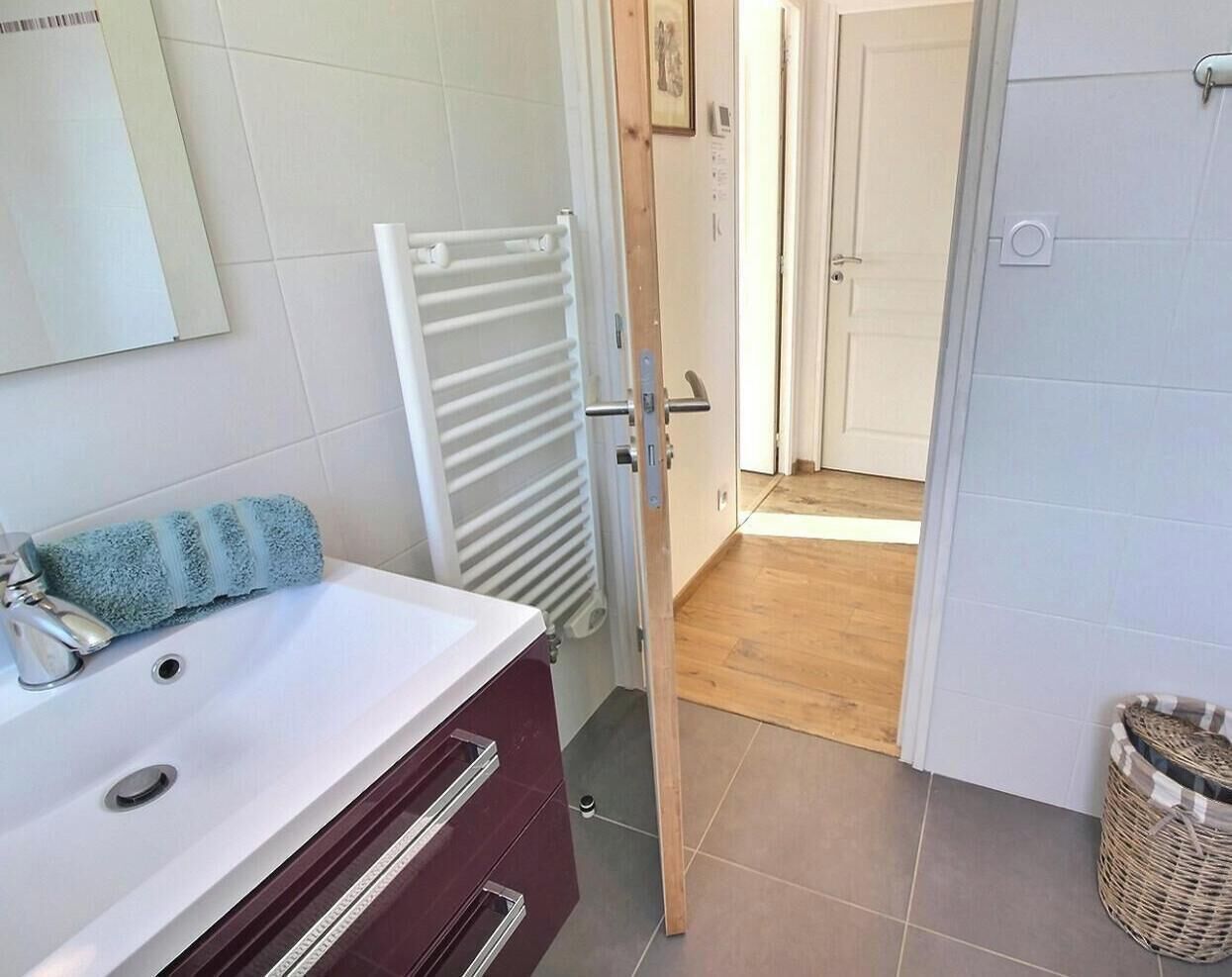 A bathroom with a white sink, a towel, a white radiator, and a wooden floor leading to a door.