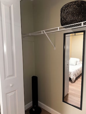 Ein Zimmer mit einer weißen Tür, einer schwarzen Stehlampe, einem weißen Wandregal und einem Spiegel, der ein Bett mit weißer Bettwäsche reflektiert.