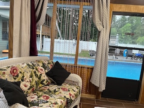 Ein Zimmer mit einer Sitzecke, einem Fenster mit Blick auf einen Swimmingpool und einer Holzterrasse.