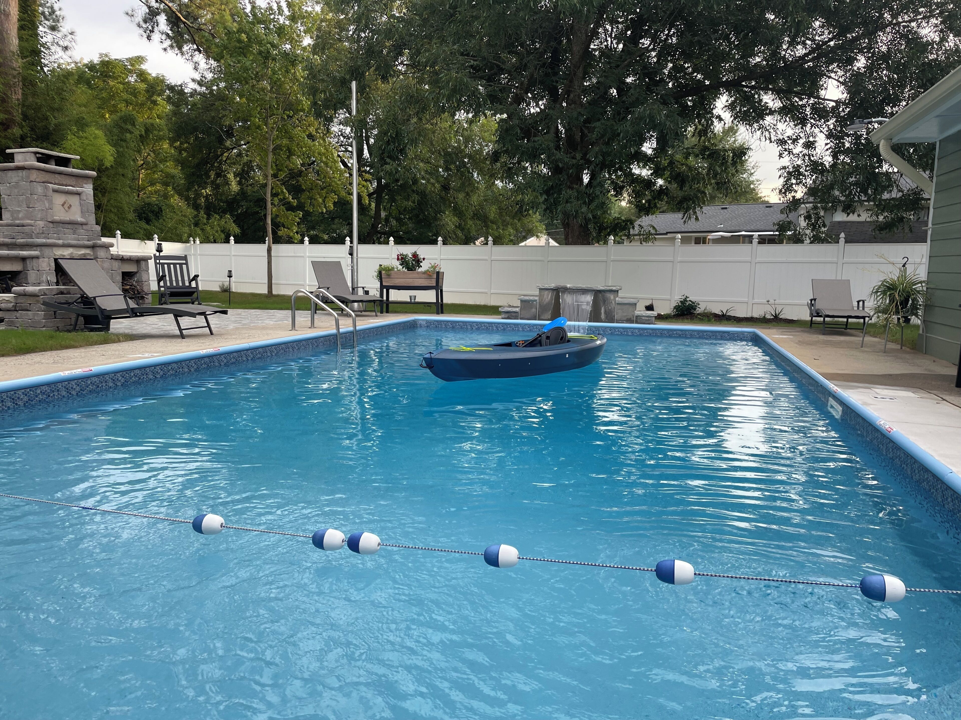 Une piscine rectangulaire aux parois bleues, entourée d’une clôture blanche, et un petit bateau au centre.