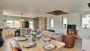 A modern dining area with a wooden table set for six, surrounded by chairs. A stone wall and a television are visible in the background. - La Stabue - LANFAINS (LANFAINS)