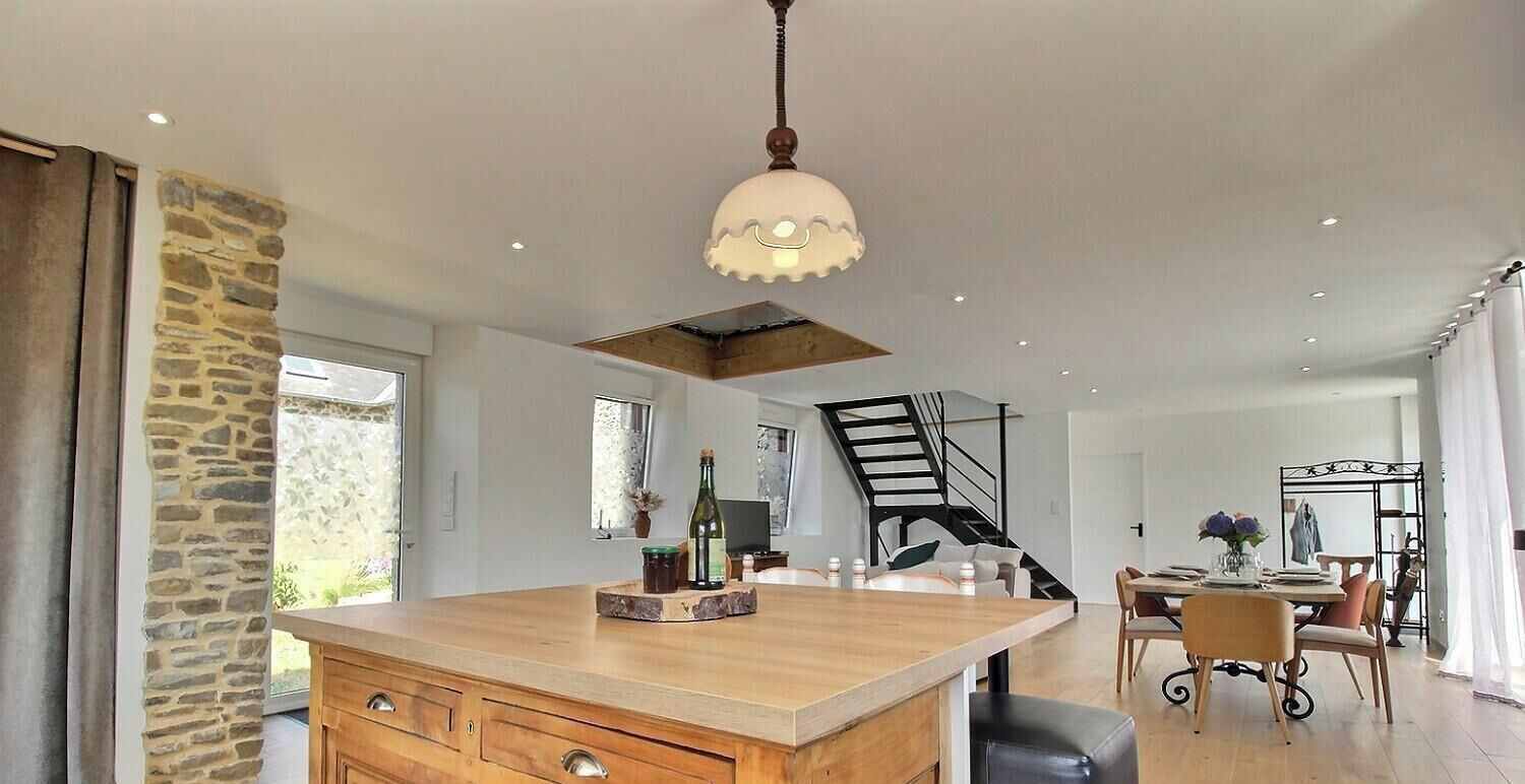 A modern kitchen with a central island, a staircase, and a dining area with chairs and a table.