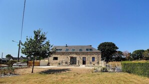 A stone building with a flat roof and multiple windows, surrounded by a grassy area and trees. - La Stabue - LANFAINS (LANFAINS)
