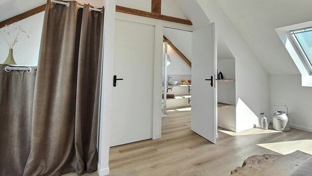 A loft bedroom with a sloped ceiling, wooden beams, a skylight, and a view to a kitchen area. - La Stabue - LANFAINS (LANFAINS)