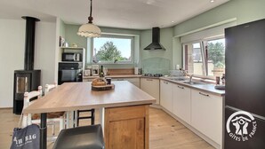 A modern kitchen with a central island, a built-in stove, and a large window providing natural light. - La Stabue - LANFAINS (LANFAINS)