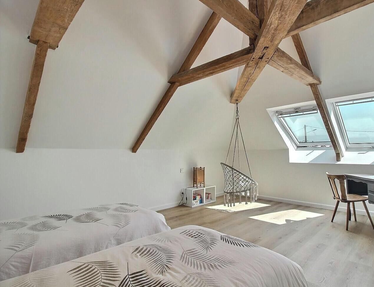 A room with a sloped ceiling, wooden beams, a desk, and a hanging chair.