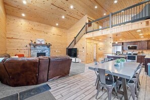 A spacious living area with a fireplace, a sofa, and a dining table with chairs. - Steelhead-Modern Yellowstone Cabin, Fiber Wi-Fi & Pine Views & Air Conditioning! (Island Park)