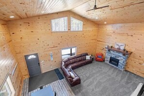 Ein Holzblockhaus-Innenraum mit Ecksofa, Kamin und zwei Fenstern.