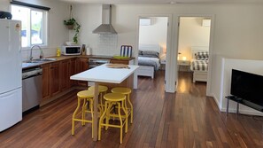 Cocina compacta con armarios de madera, una encimera blanca y un conjunto de taburetes de bar.