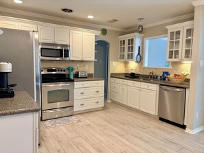 A modern kitchen with stainless steel appliances, white cabinetry, and a patterned rug. - Coastal Garden: 1 Block to Stewart Beach, 4BR Sleeps 12, Luxury Bidets (Galveston)
