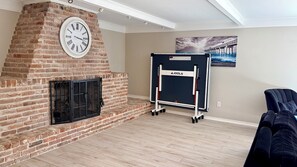 Une pièce avec une cheminée en briques, une horloge, un écran de projection et un tableau représentant une jetée.
