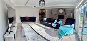 Ein Wohnzimmer mit Sofa, Fernseher, Kamin und Blick ins Freie.