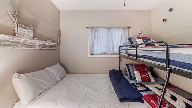 Een kleine kamer met een stapelbed, een raam met gordijnen en een plafondventilator.