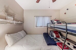 Une petite pièce avec un lit superposé, une fenêtre avec des rideaux et un ventilateur de plafond.