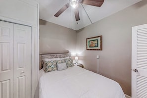 Een slaapkamer met een bed, een plafondventilator, een nachtkastje met een lamp en een lijst met een foto aan de muur.