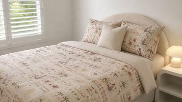 A bedroom with a bed, two pillows, a bedside table with a lamp, and a window with blinds.