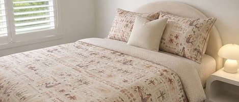 A bedroom with a bed, two pillows, a bedside table with a lamp, and a window with blinds.