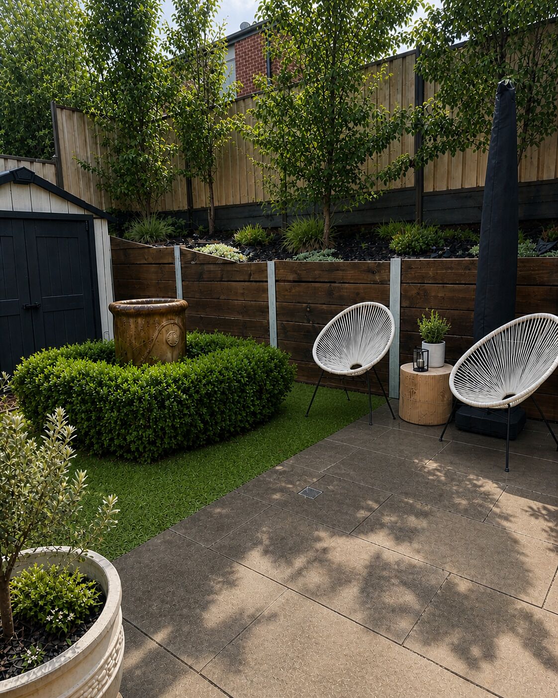 A patio area with a wooden fence, a black shed, and two white wicker chairs.
