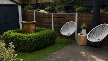 A patio area with a wooden fence, a black shed, and two white wicker chairs.
