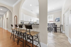 A spacious kitchen with white cabinets, a dining area with a table and chairs, and a bar area with stools. - Sleeps 15 | Walk to UF, Downtown + 50+ Restaurants (Gainesville)