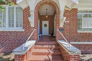 A brick house with a front porch, a door with a wreath, and a mailbox. - Sleeps 15 | Walk to UF, Downtown + 50+ Restaurants (Gainesville)