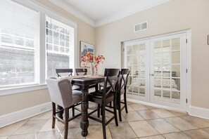 A dining area with a table and chairs, a vase with flowers, and a door with a view. - Sleeps 15 | Walk to UF, Downtown + 50+ Restaurants (Gainesville)