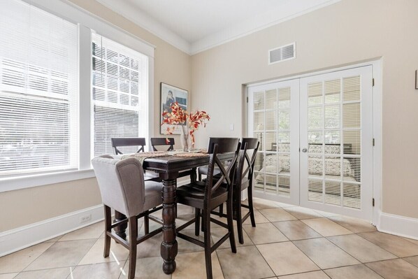 A dining area with a table and chairs, a vase with flowers, and a door with a view.