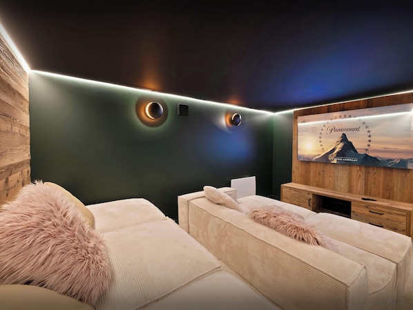 A modern room with a dark green wall, a mounted television, and a cozy seating area with a fluffy pillow.