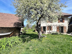 Ein rustikales Haus mit Steinwand, Holztür und einem Garten mit Gras und Blumen.