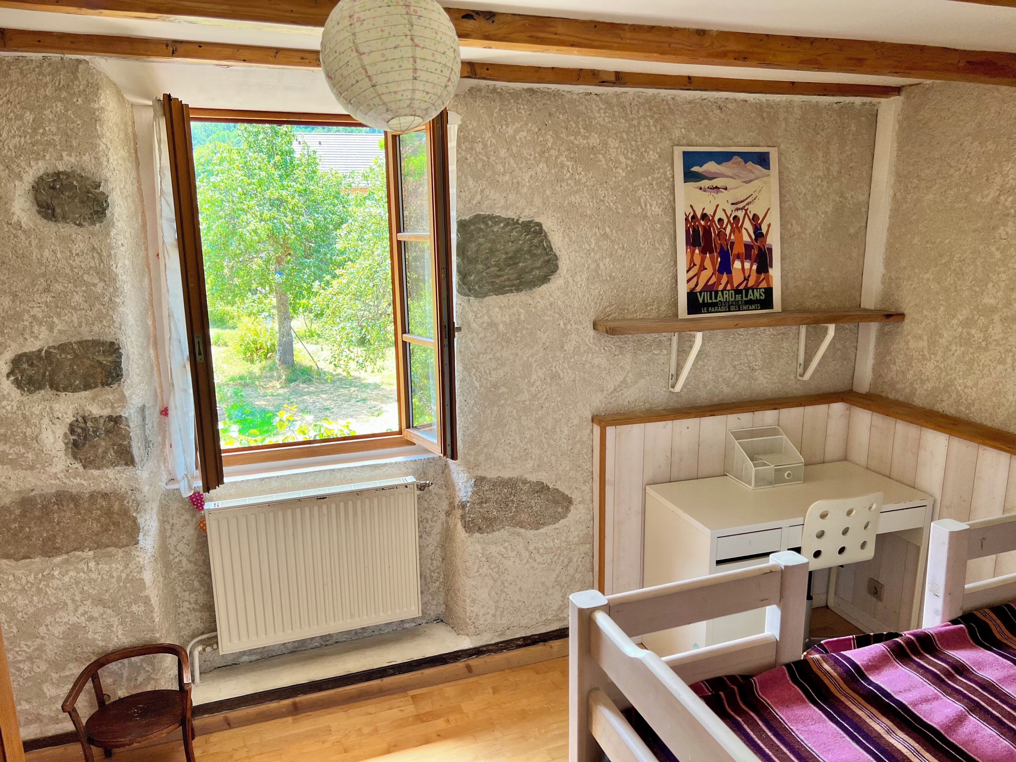 Une pièce avec une fenêtre, un radiateur, un lit, un bureau et une affiche accrochée au mur.