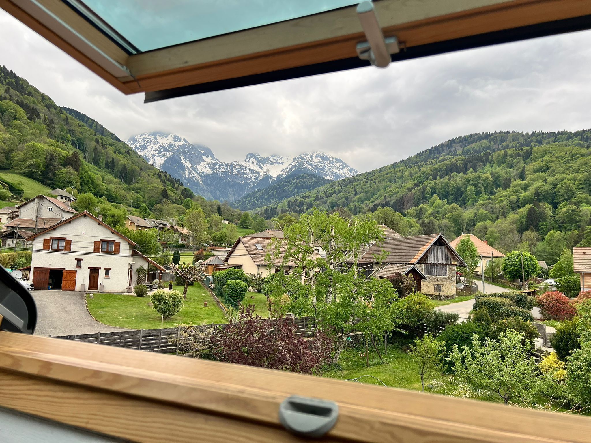 A view from a window overlooking a village with traditional houses and a mountain range in the background.