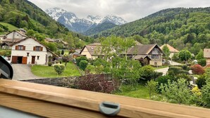 Vista da janela sobre uma aldeia com casas tradicionais e uma cordilheira ao fundo.