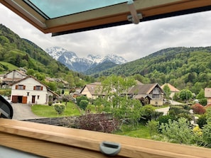 Blick aus einem Fenster auf ein Dorf mit traditionellen Häusern und einer Bergkette im Hintergrund.