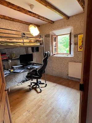 Ein kleines Zimmer mit Etagenbett, Schreibtisch inklusive Computer, Stuhl und Fenster mit Blick auf Grünflächen.